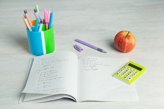 Doing homework. Notebook with math assignment, apple and stationery on white desk