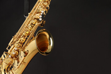 Obraz premium Jazz. One beautiful saxophone hanging from strap on black background, closeup. Space for text