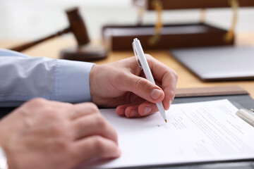 Notary signing document at table in office, closeup