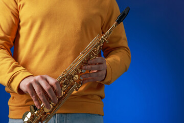 Professional musician with soprano saxophone on blue background, closeup