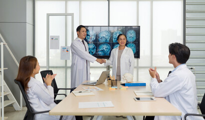 Two doctors shaking hand happily in a meeting with colleagues clapping.