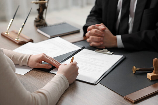 Client signing notarial document during meeting with lawyer at wooden table indoors, closeup