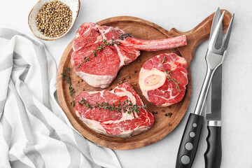 Pieces of raw beef, spices and cutlery on light grey table, flat lay