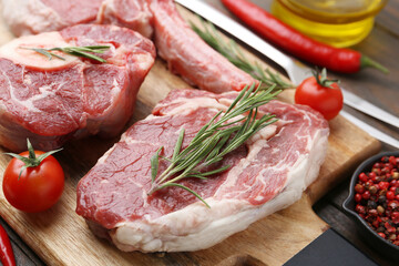 Pieces of raw beef, spices and tomatoes on wooden table, closeup
