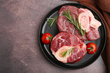Pieces of raw beef, rosemary and tomatoes on brown textured table, top view. Space for text