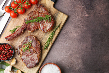 Pieces of delicious beef meat, spices and tomatoes on brown table, top view. Space for text