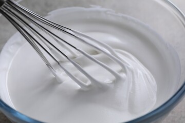 Whisking whipped cream in bowl on grey table, closeup