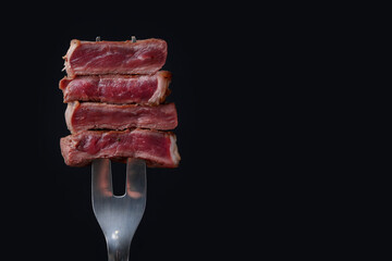 Carving fork with pieces of delicious beef meat on black background, closeup. Space for text