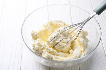 Bowl with whisk and whipped cream on white wooden table, closeup