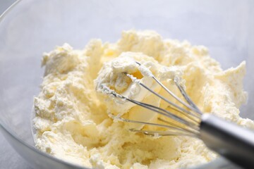 Bowl with whisk and whipped cream on grey table, closeup