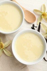 Tasty condensed milk, vanilla pods, flowers and spoon on white wooden table, flat lay