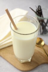Delicious vanilla milk in glass, pods and spoon on grey table, closeup