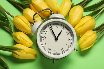 Spring time. Alarm clock and beautiful tulips on green background, flat lay