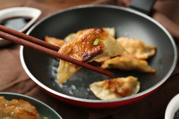 Taking tasty fried gyoza (dumpling) with chopsticks on wooden table, closeup