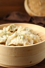 Tasty boiled gyoza (dumplings) in bamboo steamer on wooden table, closeup