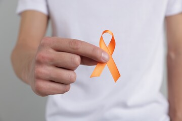 Multiple Sclerosis awareness. Man with orange ribbon on light grey background, closeup