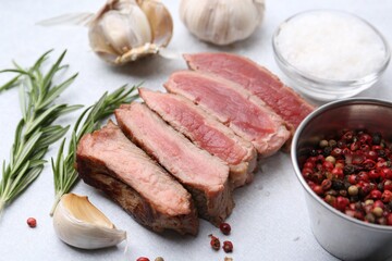 Delicious sliced beef tenderloin with different degrees of doneness and spices on light table, closeup