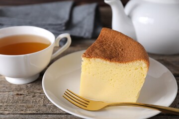 Piece of tasty Japanese Castella sponge cake, tea and fork on wooden table, closeup
