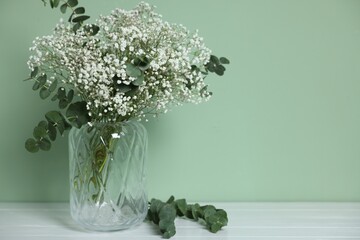 Beautiful gypsophila flowers and eucalyptus branches in vase on white table against turquoise background. Space for text