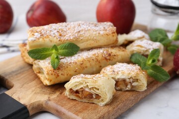 Tasty apple strudels with powdered sugar and mint on white marble table, closeup