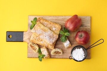 Tasty apple strudels with powdered sugar, fruits and mint on yellow background, top view