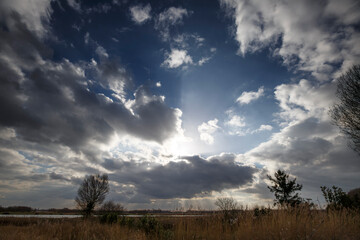 Dramatic clouds illuminate the sky above a tranquil landscape at dusk near a quiet lake in the countryside