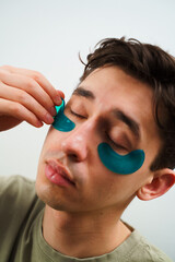 Young man with sensitive skin wears hydrogel patches under his eyes. Male skincare routine at home.