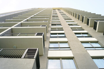 Fototapeta premium Facade of a modern multi-story residential building: bottom-up view of the outer wall with balconies, air conditioners hidden behind grilles, and windows. Buying real estate in a new area.