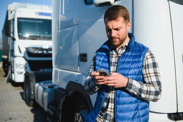 Professional driver using mobile phone while standing in front of his truck. Copy space