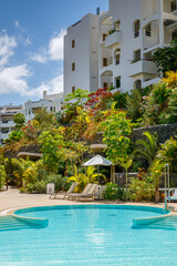 Resort pool area featuring turquoise water in the pool and lush greenery. Sun loungers and umbrella create a relaxing atmosphere