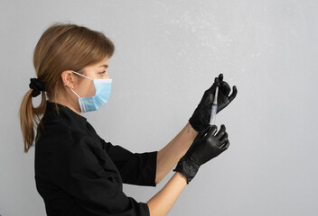 A professional cosmetologist wearing gloves and a mask carefully prepares a syringe filled with...
