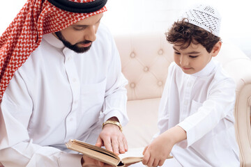 Arabian bearded man is reading book with small son.