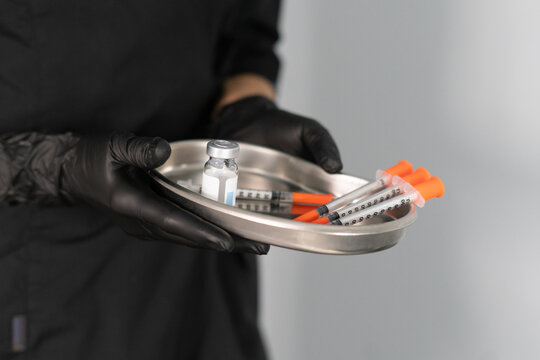 A cosmetologist organizes multiple syringes and a vial in a tray, preparing for a botox injection in a sleek, well-lit clinic.