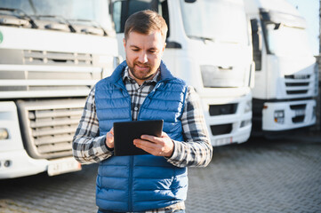 Happy confident male driver standing in front on his truck, using his tablet