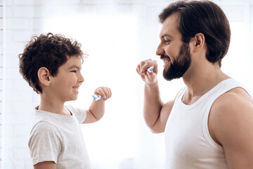 Happy father and son brush teeth, looking at each other.