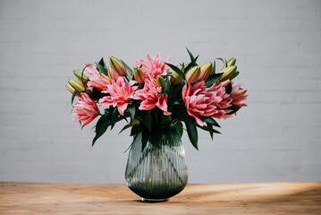 A vase of pink flowers sits on a wooden table. The flowers are arranged in a way that they are all facing the same direction, creating a sense of harmony and balance. The vase itself is clear