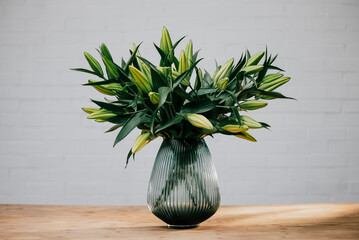 A vase of green flowers sits on a wooden table. The flowers are in a tall, narrow vase and are arranged in a way that makes them look like they are reaching up towards the ceiling