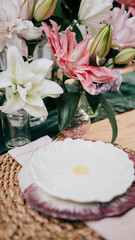 A table with a white plate and a vase of pink flowers. The flowers are arranged in a vase and are placed on a table