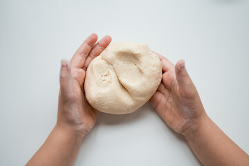 Child hands kneading dough on white surface