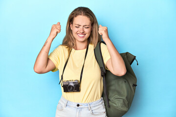 Fototapeta premium Young blonde traveler with camera and backpack in studio covering ears with hands.
