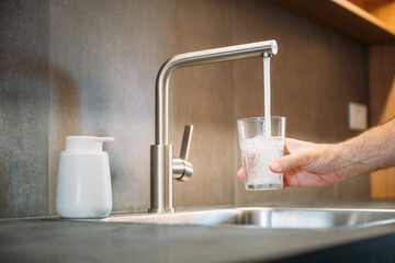 Man pouring tap water from kitchen faucet into drinking glass
