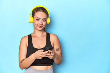 Young blonde sportswoman wearing yellow headphones in a studio