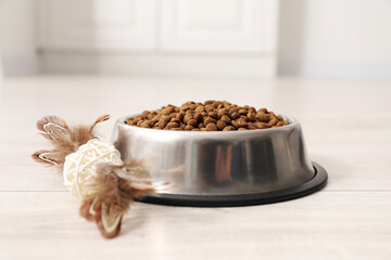 Dry pet food granules in feeding bowl and cat toy on floor indoors