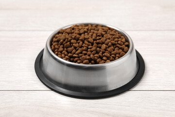 Dry pet food granules in feeding bowl on floor