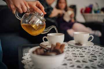 Woman pouring herbal tea into tea cup on coffee table