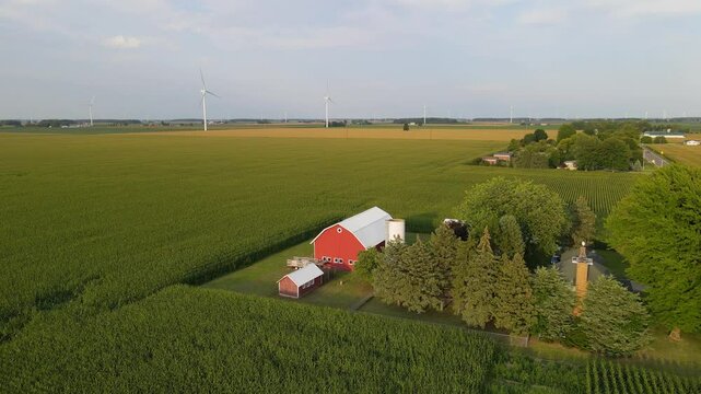Orbiting view of a traditional farm house with a red barn and silo with wind turbines in the background