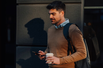 Businessman walking and using smartphone with coffee in hand