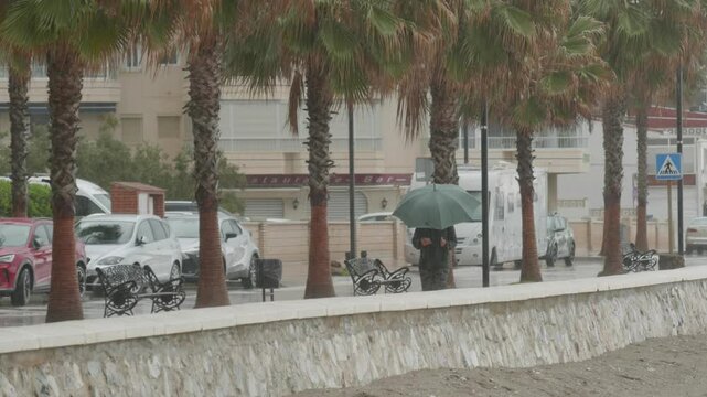 HOMBRE PASEA POR EL PASEO MARITIMO CON UN PARAGUAS EN UNA BORRASCA