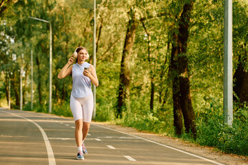 Sporty woman jogging in a serene park trail during a sunny afternoon © Bliss