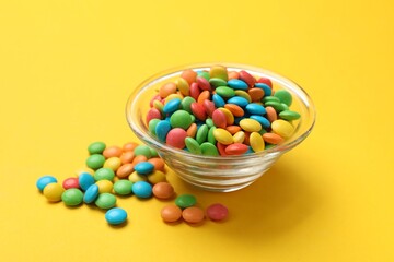 Tasty candies in bowl on yellow background, closeup